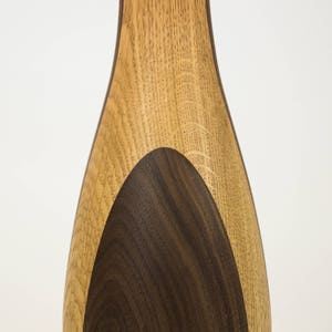 May include: A wooden vase with a light brown exterior and a dark brown oval inlay. The vase is made of two different types of wood.