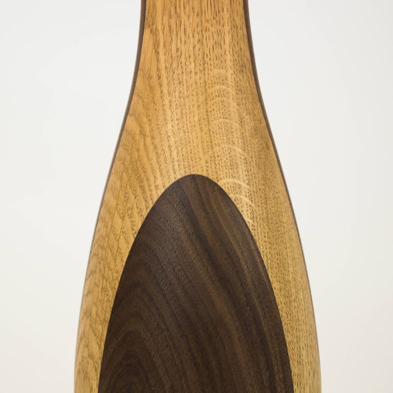 May include: A wooden vase with a light brown exterior and a dark brown oval inlay. The vase is made of two different types of wood.