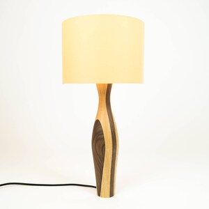 May include: A wooden table lamp with a light brown and dark brown patterned base and a cream-colored lampshade.