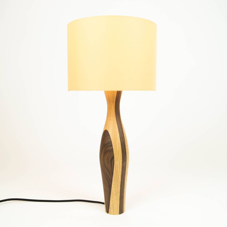 May include: A wooden table lamp with a light brown and dark brown patterned base and a cream-colored lampshade.