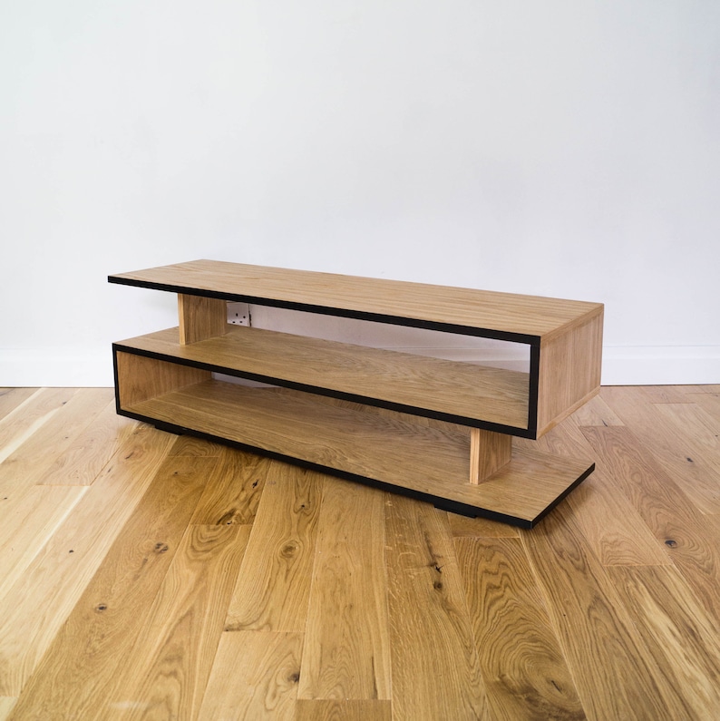 May include: A wooden TV stand with two shelves and black trim. The stand is made of light wood and has a modern design.