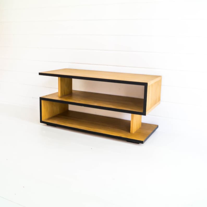 May include: A wooden two-tiered shelf unit with black trim. The shelf is made of light wood and has a modern design.