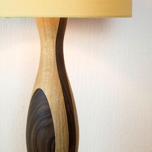 May include: Close-up of a wooden lamp base with a light brown and dark brown wood grain pattern. The lamp base is shaped like a vase and has a smooth, polished finish.