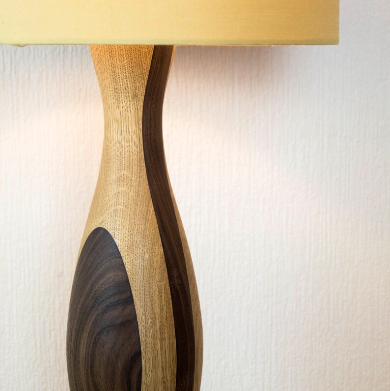 May include: Close-up of a wooden lamp base with a light brown and dark brown wood grain pattern. The lamp base is shaped like a vase and has a smooth, polished finish.
