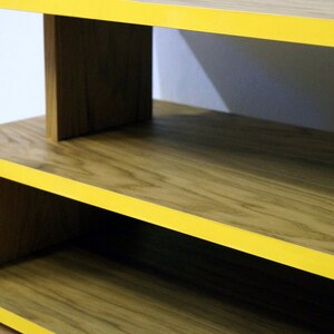 May include: A wooden shelf unit with yellow trim. The shelf has two levels and is made of natural wood with a visible grain pattern.