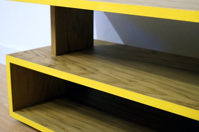 May include: A wooden shelf unit with yellow trim. The shelf has two levels and is made of natural wood with a visible grain pattern.