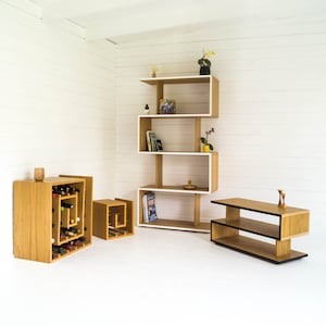May include: A set of three wooden shelves with a white top and black accents. The shelves are arranged in a staggered pattern and are filled with books, plants, and decorative items. The shelves are made of a light wood and have a modern design.