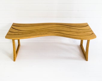 May include: A wooden coffee table with a wavy top and a natural wood finish. The table has a simple, modern design and is supported by two legs on each side.