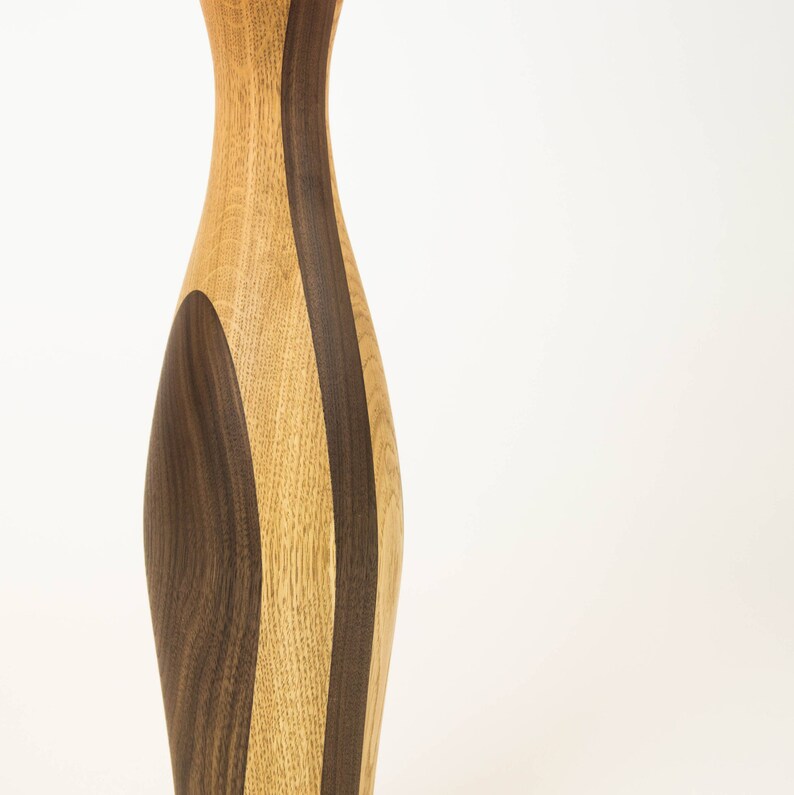 May include: A wooden vase with a unique design featuring alternating strips of light and dark wood.