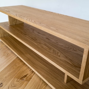May include: A light wood shelf unit with two shelves. The shelves are made of solid wood and have a natural finish. The unit is freestanding and has a simple, modern design.