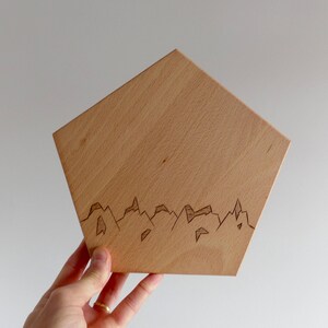 May include: A wooden plaque with a geometric design, featuring a mountain range silhouette etched into the surface.