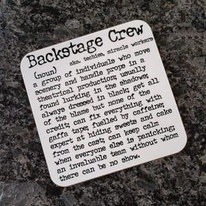 May include: A white square coaster with black text defining "Backstage Crew" as a group of individuals who work behind the scenes in theatrical productions. The text describes their responsibilities, including moving scenery, handling props, and keeping calm when others panic.