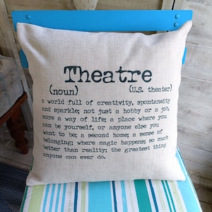 May include: A beige square cushion with the word "Theatre" printed in black, along with a definition. The cushion is on a chair with blue and white stripes. The definition describes theatre as a world of creativity.
