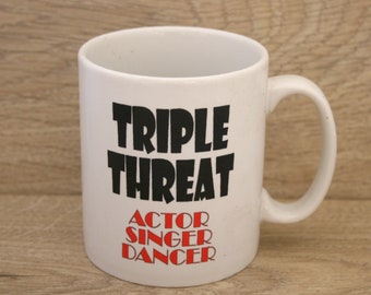 May include: White ceramic mug with black text that reads "Triple Threat" and red text that reads "Actor Singer Dancer".