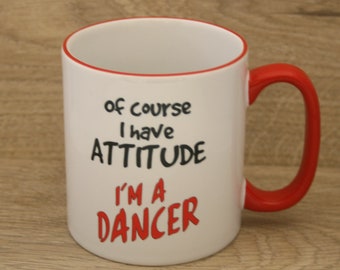 May include: White ceramic mug with a red rim and handle. The mug has black text that reads "Of course I have attitude I'm a dancer" with the words "I'm a" in red.
