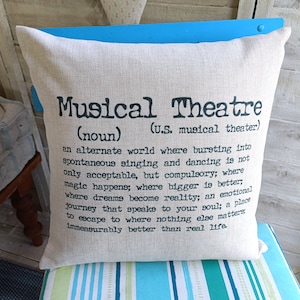 May include: A beige cushion with black text that reads "Musical Theatre (noun) (U.S. musical theatre) an alternate world where bursting into spontaneous singing and dancing is not only acceptable, but compulsory; where magic happens; where bigger is better; where dreams become reality; an emotional journey that speaks to your soul; a place to escape to where nothing else matters; immeasurably better than real life."