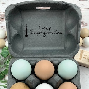 May include: A gray cardboard egg carton with six brown eggs, two blue eggs, and one white egg. The carton has a black thermometer and the words 
