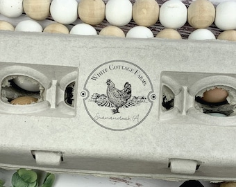 May include: A light gray egg carton with the text "WHITE COTTAGE FARMS" and a hen illustration. The carton contains several brown eggs. A wooden stamp and decorative wooden beads are also visible.