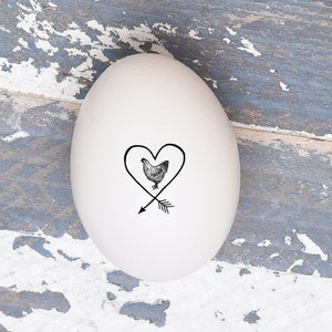 May include: A white egg with a black and white drawing of a chicken inside a heart with an arrow through it.