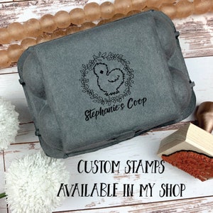May include: A grey cardboard egg carton with a black and white custom stamp featuring a chicken silhouette inside a floral wreath. The stamp reads "Stephanie's Coop". The text "CUSTOM STAMPS AVAILABLE IN MY SHOP" is printed below the carton.