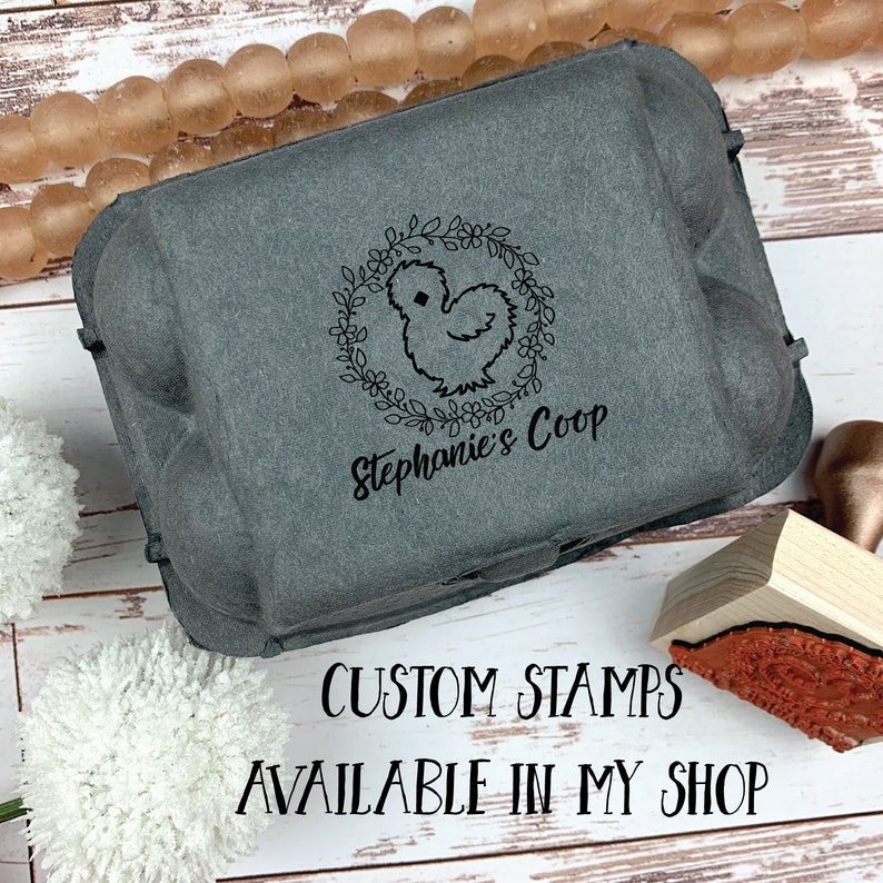 May include: A grey cardboard egg carton with a black and white custom stamp featuring a chicken silhouette inside a floral wreath. The stamp reads "Stephanie's Coop". The text "CUSTOM STAMPS AVAILABLE IN MY SHOP" is printed below the carton.