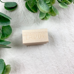 May include: A wooden stamp with the words "LAID ON:" carved into the surface.