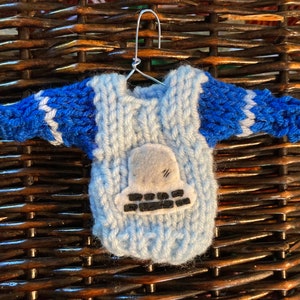 Op de afbeelding: Een kleine blauwe en witte gebreide trui met een vilten applicatie van een ruimteschip op de voorkant.