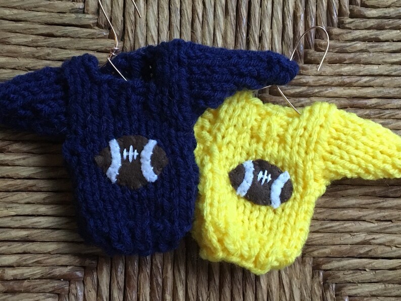 Op de afbeelding: Twee gebreide truien met voetbalmotieven. De ene trui is donkerblauw en de andere is geel.