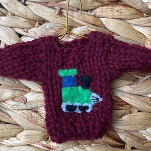 May include: A maroon knitted sweater ornament with a green, blue and black felt train appliqué.