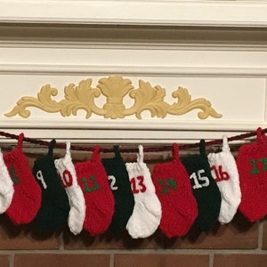 May include: A Christmas advent calendar made of knitted stockings with numbers 1 through 24. The stockings are hung on a string and are red, white, and green.