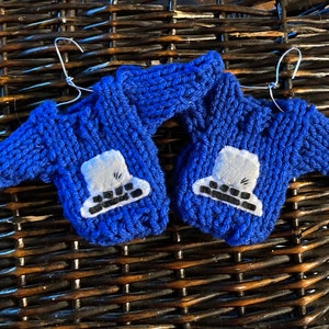May include: Two blue knitted sweaters with white and black keyboard designs hanging on wire hangers.