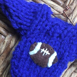 Op de afbeelding: Een blauwe gebreide trui met een bruine en witte vilt voetbal applicatie.