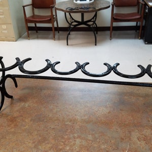 May include: Black metal boot rack made from horseshoes. The rack has five horseshoe slots and two horseshoe legs.