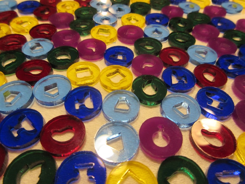 K&ouml;nnte beinhalten: Eine Sammlung von bunten, runden, aus Kunststoff gefertigten Spielmarken mit verschiedenen Symbolen in der Mitte. Die Spielmarken sind in verschiedenen Farben, darunter Rot, Blau, Gr&uuml;n, Gelb und Lila.