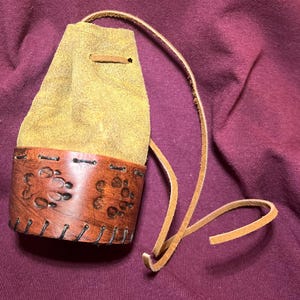 May include: A white ceramic mug with a black handle and the text "But First, Coffee" in a bold, black font. The mug is set against a blurred background, suggesting a cozy setting.