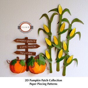 Op de afbeelding: Een paper piecing collectie met een pompoenveld scène. Het ontwerp omvat twee oranje pompoenen, een houten wegwijzer met aanwijzingen en maïsstengels met gele korrels. Tekst op het bord luidt "pumpkin patch", "corn maze" en "hayride".
