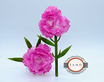 May include: Two pink carnations with white centers, made from paper, are attached to a green stem. The flowers are arranged in a bouquet. The image is labeled "Carnation Paper Piecing Patterns" and includes the logo "ForAvaMoreDesigns" with the abbreviation "FAMD".