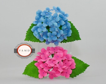 Peut inclure: Deux fleurs d'hortensia en papier, une bleue et une rose, chacune avec des feuilles de papier vertes. Les fleurs sont étiquetées "3D Hydrangea Paper Piecing Patterns" et proviennent de ForAvaMoreDesigns.