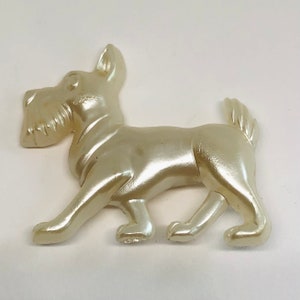 May include: A white ceramic figurine of a dog walking. The dog has a long snout and a fluffy tail.