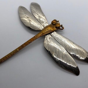 Puede incluir: Un broche de lib&eacute;lula de plata con cuerpo de cobre y alas detalladas.