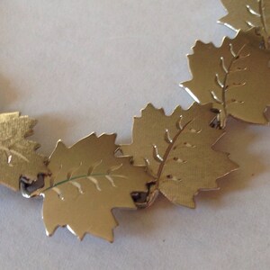 May include: A silver bracelet with a chain made of linked maple leaf charms. Each leaf has a detailed etched design.