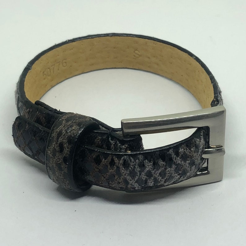 May include: A black leather belt with a silver buckle. The belt has a snakeskin pattern and the number 50776 is printed on the inside of the belt.