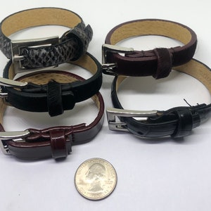 May include: Four leather bracelets with silver buckles. The bracelets are stacked on top of each other. The bracelets are in different colors, including black, brown, and gray.