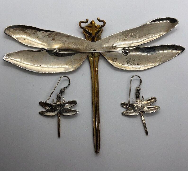 Puede incluir: Un broche de lib&eacute;lula de plata con detalles dorados y pendientes a juego. El broche est&aacute; firmado "Country" en la parte posterior.