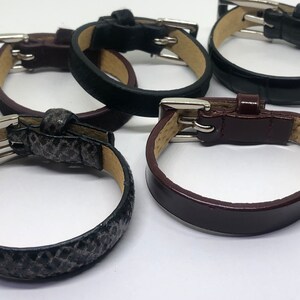 May include: Four leather bracelets with silver buckles. The bracelets are in different colors and textures, including black, brown, and gray.