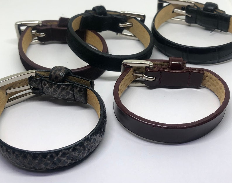 May include: Four leather bracelets with silver buckles. The bracelets are in different colors and textures, including black, brown, and gray.