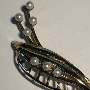 May include: A gold-toned brooch with a leaf design and pearl accents. The brooch features a delicate, openwork design with multiple pearl embellishments.