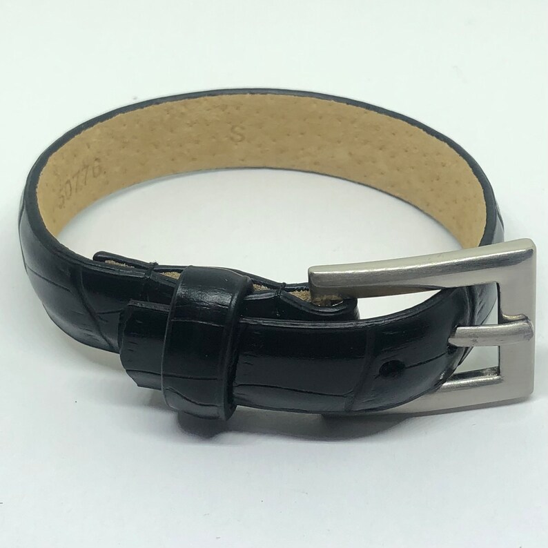 May include: A black leather watch band with a silver buckle. The band has a crocodile pattern and the buckle has a simple design.