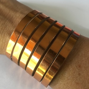 May include: A gold-toned copper bracelet made of multiple stacked bands.