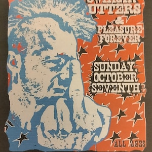 May include: Concert poster for The Damned with Swingin' Utters and Pleasure Forever at the Bluebird Theatre in Denver, CO. The poster features a blue and white illustration of a person giving the middle finger, set against an orange and black background.